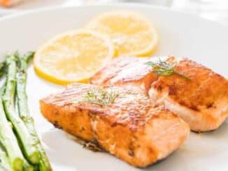 two salmon fillets, two lemon slices and asparagus on a white plate