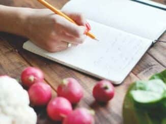 hand writing in a recipe notebook surrounded by fresh produce