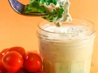 Low Sodium Ranch Dressing in a jar surrounded with tomatoes, cucumbers and celery. A fork with a lettuce leaf dipped in the dressing