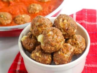 meatballs in a small white bowl on a red and white checked napkins with a pot of meatballs in sauce behind