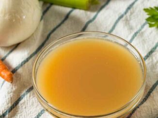 chicken broth in a clear glass bowl on a white striped kitchen towel with vegetables