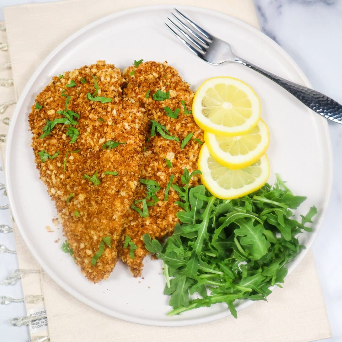 breaded chicken cutlets on plate with arugula and lemon slices